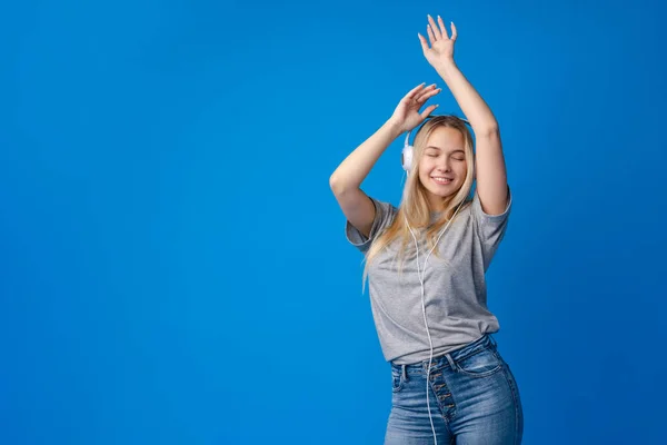 Glad ung kvinna med hörlurar på en blå bakgrund — Stockfoto