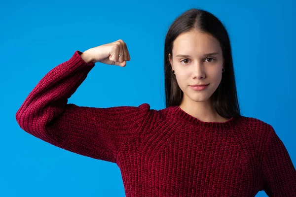 Vacker ung kvinna som visar sin muskulatur och tittar på kameran på blå bakgrund — Stockfoto