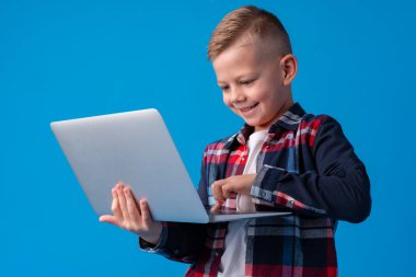 Mavi arka planda dizüstü bilgisayarı olan zeki bir çocuk.