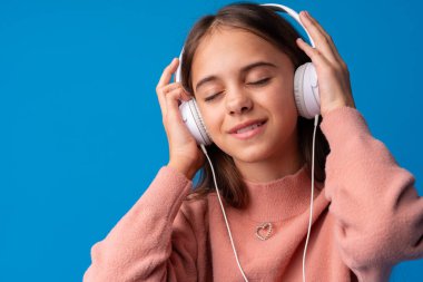 Kulaklıklı liseli kız mavi arka planda müzik dinliyor.