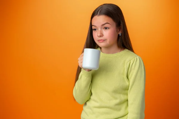 Uykulu genç kız elinde turuncu arka planda sıcak bir fincan kahve tutuyor. — Stok fotoğraf