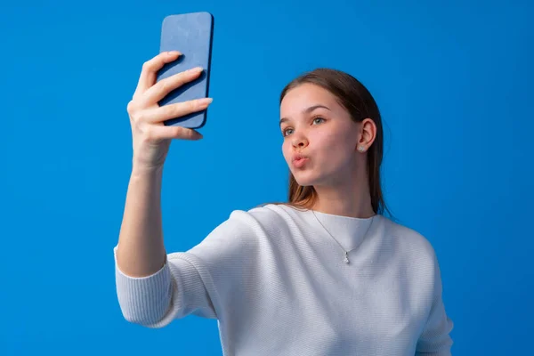 Glückliche junge Frau macht Selfie vor blauem Hintergrund — Stockfoto