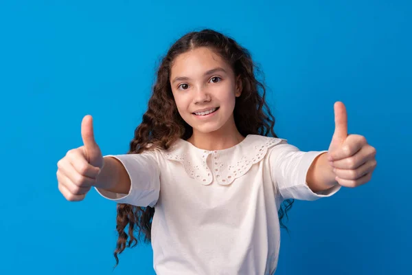Porträtt av tonåring flicka att göra tummen upp gest på blå bakgrund — Stockfoto