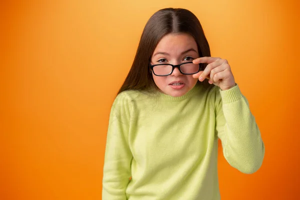在橙色背景下被隔离的眼镜中的有趣的高加索少女 — 图库照片