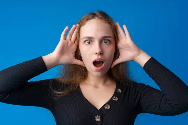 Chockad och förvånad ung tonåring flicka mot blå bakgrund — Stockfoto