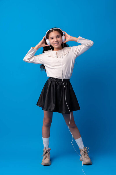 Schoolgirl with headphones listening to music against blue background