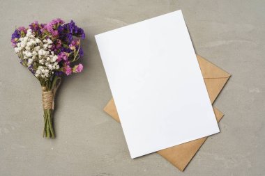 Çiçekler, boş kağıt ve zarf bir masanın üstünde.