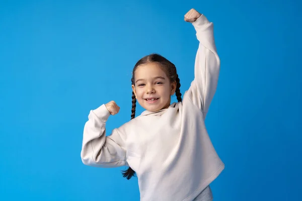 Kicsi aranyos lány mutatja erejét a kék háttér — Stock Fotó