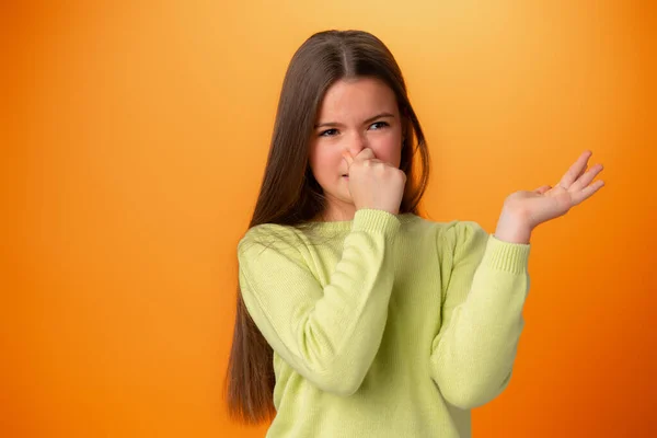 在橙色背景下闻到一股难闻的气味，所以才会抱着鼻子的少女 — 图库照片