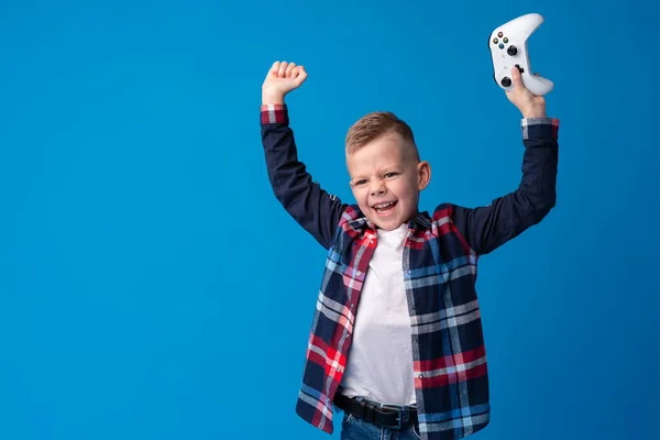 Menino se divertindo jogando com console de vídeo no fundo azul — Fotografia de Stock