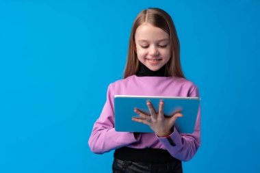 Küçük kız mavi arka planda dijital tablet kullanıyor.