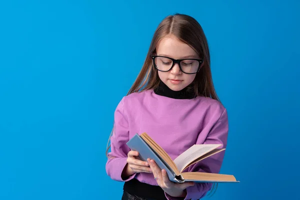 Küçük, güzel, gülümseyen kız kitabı mavi arka planda tutuyor. — Stok fotoğraf
