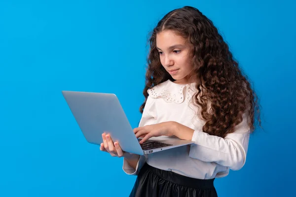 Retrato de una niña sosteniendo un ordenador portátil mientras está de pie sobre un fondo azul —  Fotos de Stock