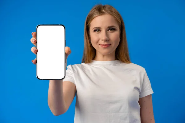 Jeune femme pointe du doigt l'écran isolé du smartphone sur fond de couleur bleue — Photo