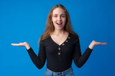 Gülümseyen genç bir kadın mavi arka planda fotokopi alanını işaret ediyor