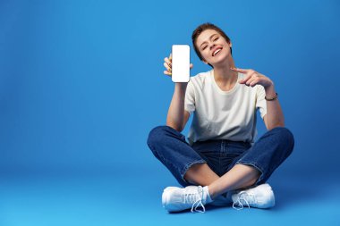 Mutlu kadın mavi arka planda boş akıllı telefon ekranı gösterir