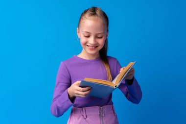 Küçük, güzel, gülümseyen kız kitabı mavi arka planda tutuyor.