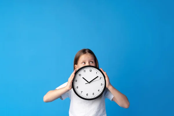 Hermosa chica adolescente sosteniendo reloj de pared sobre fondo azul — Foto de Stock