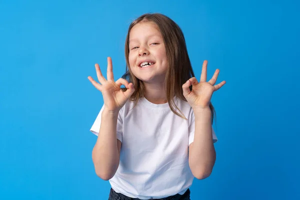 Menina bonito mostrando ok sinal no fundo azul — Fotografia de Stock