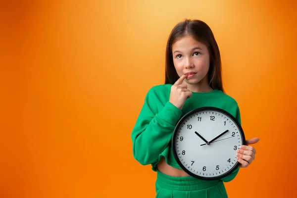 주황색 배경 위에 커다란 시계를 들고 있는 아름다운 십 대 소녀 — 스톡 사진