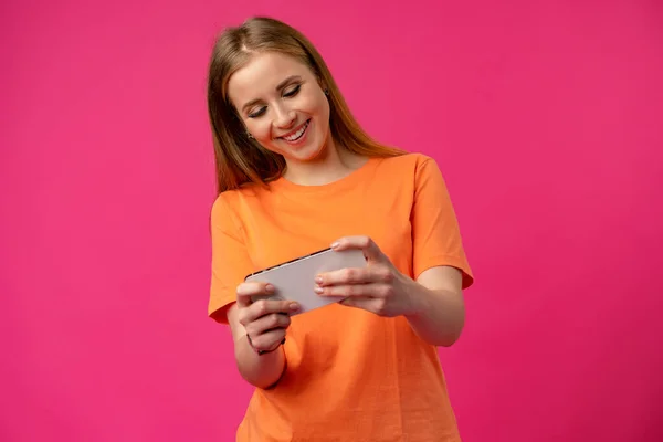 Glückliche attraktive Frau spielt Videospiel auf Smartphone auf rosa Hintergrund — Stockfoto