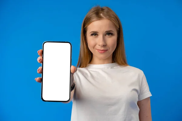 Jeune femme pointe du doigt l'écran isolé du smartphone sur fond de couleur bleue — Photo