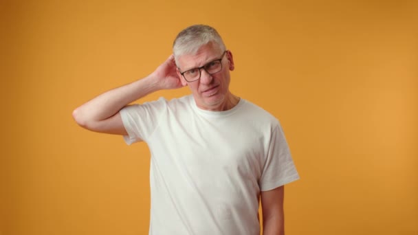 Närbild porträtt av omtänksam senior man gnugga huvudet mot gul bakgrund — Stockvideo