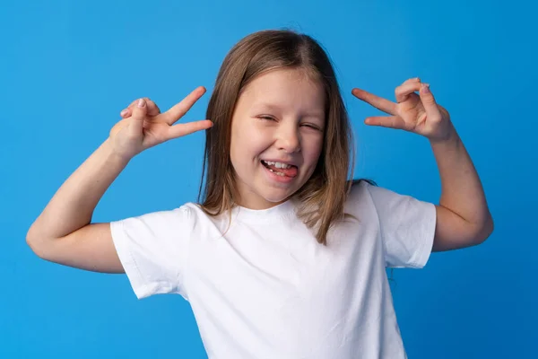 Fiatal tini lány bemutató béke szimbólum ujjak ellen kék háttér — Stock Fotó