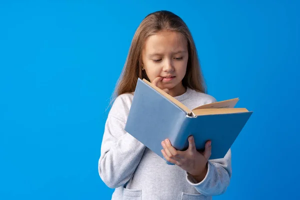Malá krásná usměvavá dívka drží knihu proti modrému pozadí — Stock fotografie