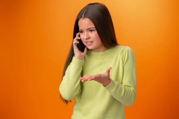 Tini lány beszél mobiltelefon elszigetelt narancs háttér — Stock Fotó