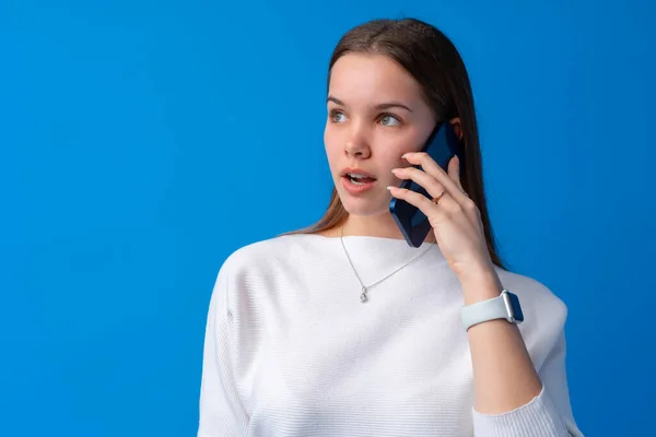 Menina adolescente bonita falando no telefone celular contra fundo azul — Fotografia de Stock