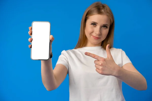 Jeune femme pointe du doigt l'écran isolé du smartphone sur fond de couleur bleue — Photo