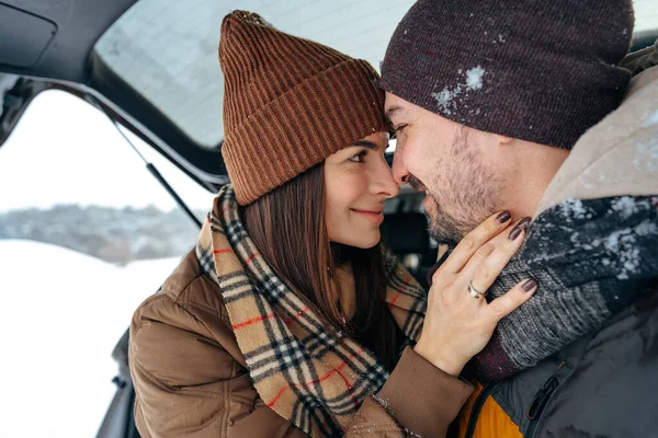 Lovely smiling couple sitting in car trunk in winter forest — Stock Photo, Image