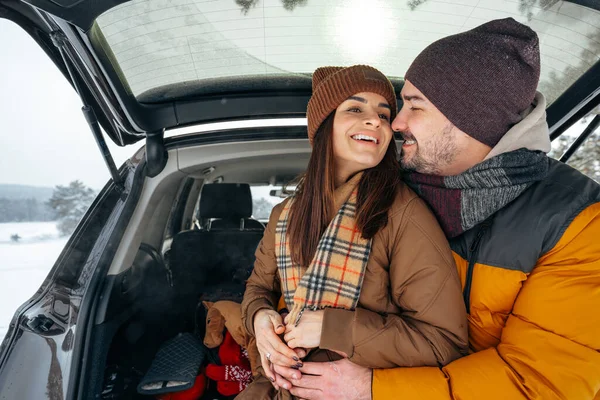 Lovely smiling couple sitting in car trunk in winter forest — Stock Photo, Image