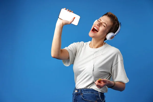 Gyönyörű fiatal nő fülhallgató hallgat zenét a kék háttér — Stock Fotó