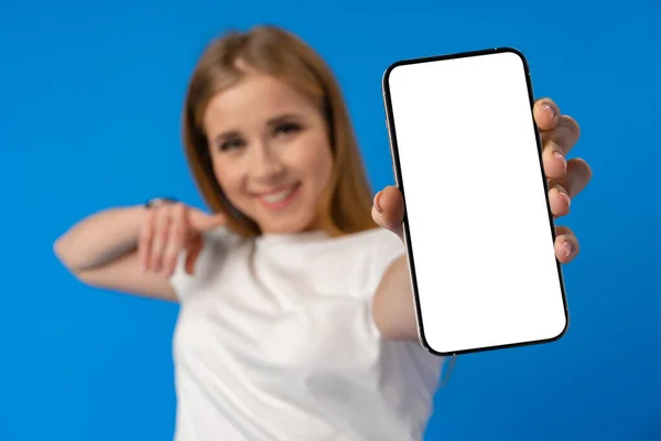 Νεαρή γυναίκα σημείο δάχτυλο σε απομονωμένη οθόνη smartphone πάνω από το μπλε χρώμα φόντο — Φωτογραφία Αρχείου