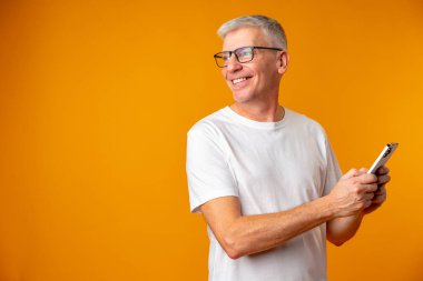 Sarı arka planda akıllı telefon kullanan kıdemli gülümseyen adam.