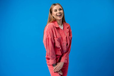 Genç bir kadın mavi arka plandaki stüdyoda neşeyle gülüyor.