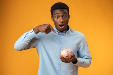 Genç Afrikalı Amerikalı adam kumbarayı sarı arka planda tutuyor.