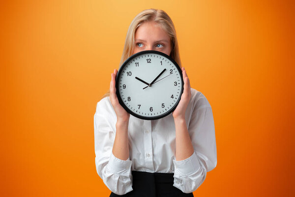 Beautiful teen girl holding big clock over orange background