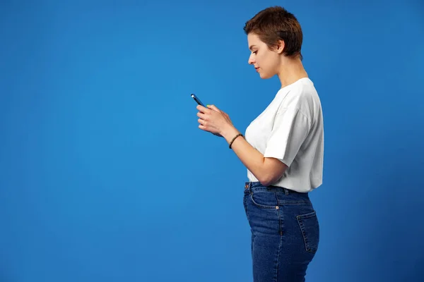 Glückliches nettes Mädchen mit Handy isoliert über blauem Hintergrund — Stockfoto