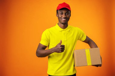 Turuncu stüdyoda üniformalı, gülümseyen siyah kurye.