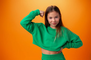 Genç kız turuncu arka planda kaslarını gösteriyor.