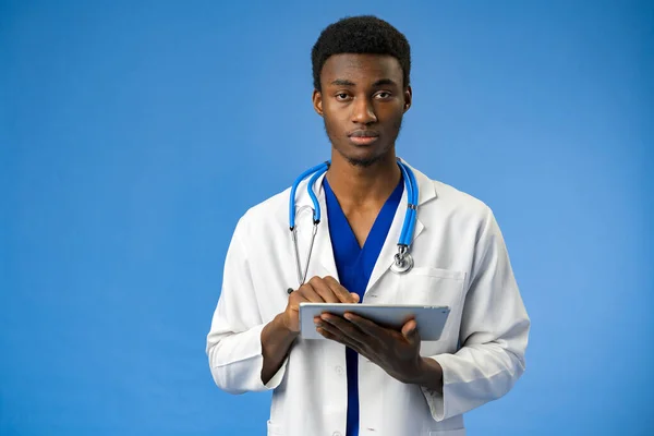 Selbstbewusster schwarzer Arzt posiert vor blauem Studiohintergrund. — Stockfoto
