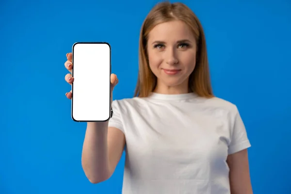 Jeune femme pointe du doigt l'écran isolé du smartphone sur fond de couleur bleue — Photo