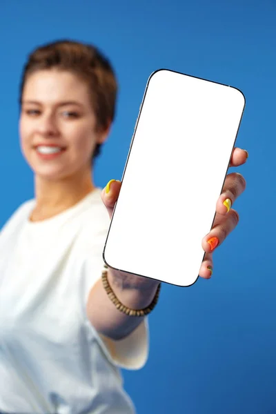 Mulher feliz mostra tela de smartphone em branco contra fundo azul — Fotografia de Stock