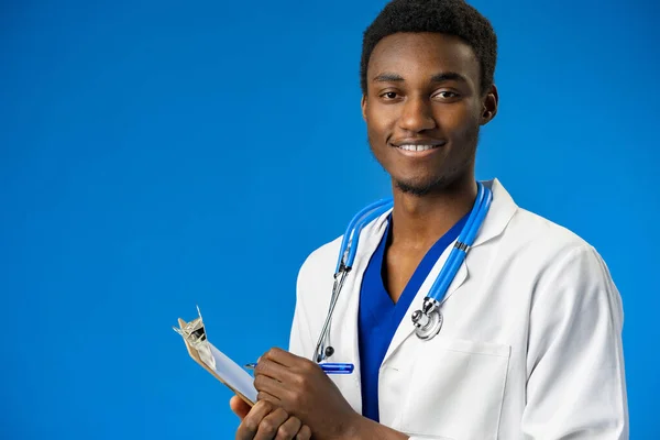 Selbstbewusster schwarzer Arzt posiert vor blauem Studiohintergrund. — Stockfoto