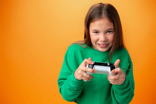 Giovane bella ragazza adolescente che gioca con console joystick su sfondo arancione — Foto Stock