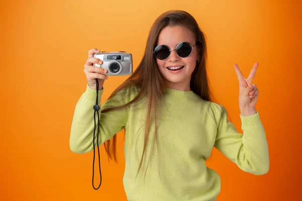 Красивая девушка-подросток со старой фотокамерой на оранжевом фоне — стоковое фото
