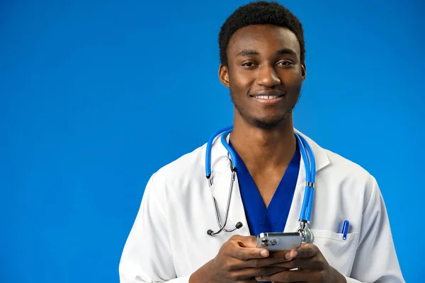 Fröhlicher afrikanischer Arzt mit Handy über blauem Studiohintergrund — Stockfoto